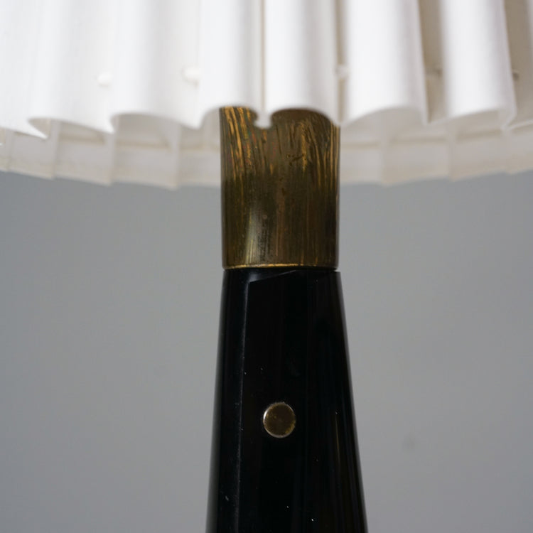 Table lamp with a white pleated shade and black base that has brass details.