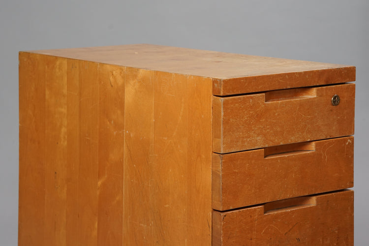 Wooden filing cabinet with four drawers, the lowest drawer being double the size of the others. The cabinet has a lock on the first drawer. Worn from use.