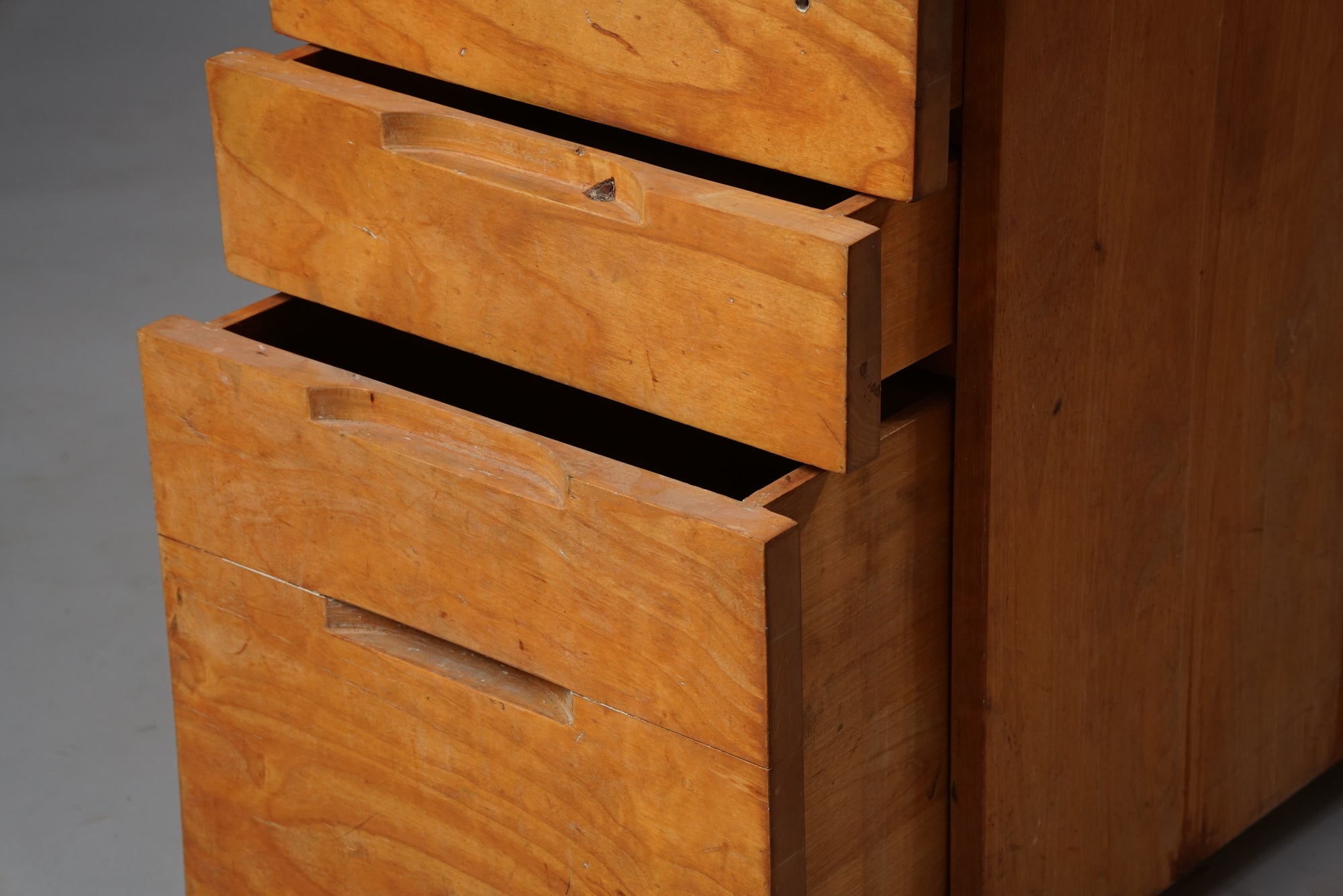 Wooden filing cabinet with four drawers, the lowest drawer being double the size of the others. The cabinet has a lock on the first drawer and four wheels. Worn from use.