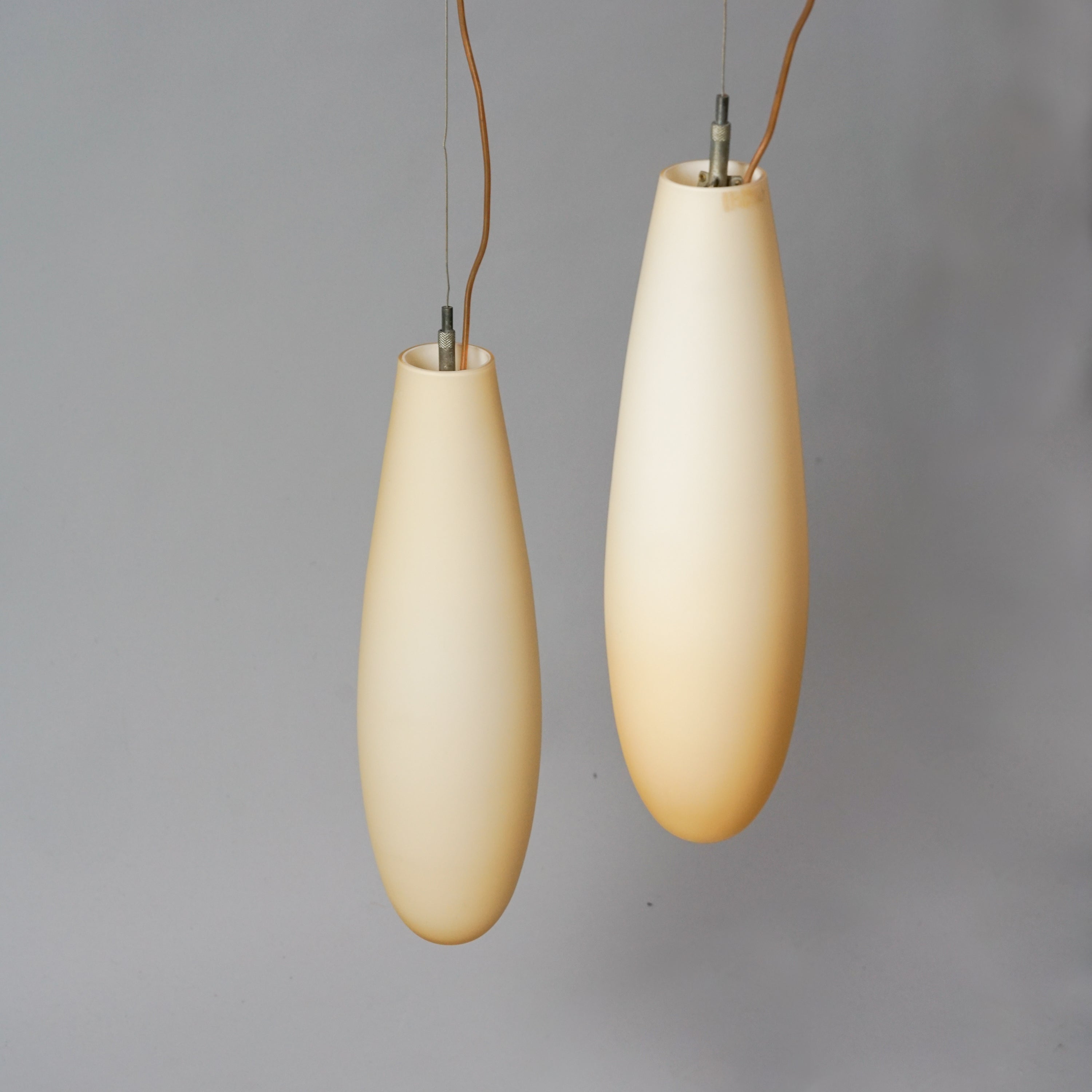 Kaksi soikean muotoista valaisinta, jotka ovat tehty kellertävän valkoisesta opaalilasista.