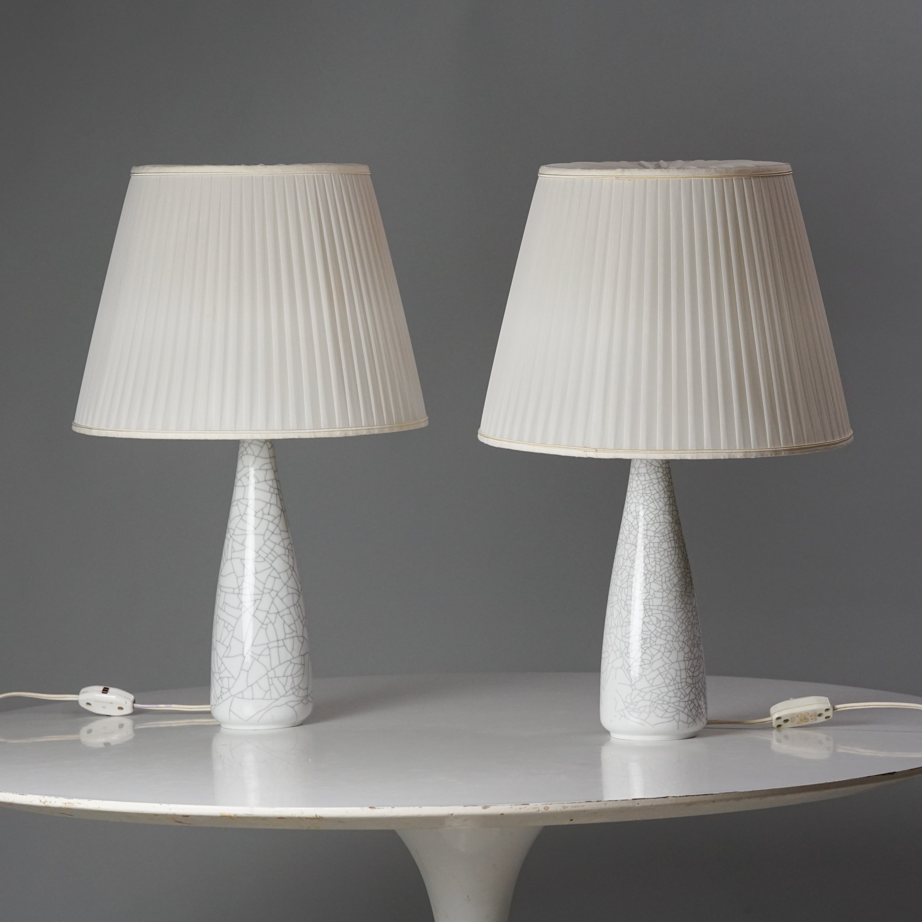 Kaksi samanlaista lamppua, joissa valkoiset laskostetut varjostimet. Lamppujen valkoisissa jaloissa on harmaa kuviointi, joka muistuttaa marmoria.
