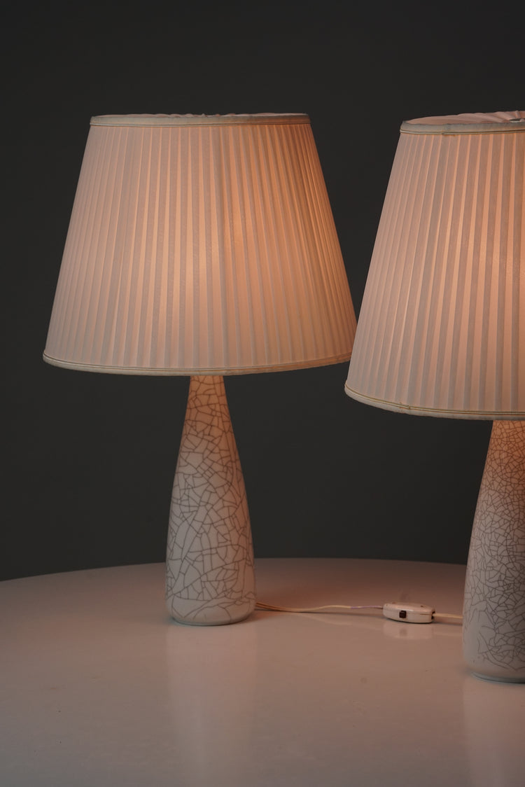 Two lamps with white pleated shades. The white bases of the lamps are decorated with a grey pattern similar to marble. 