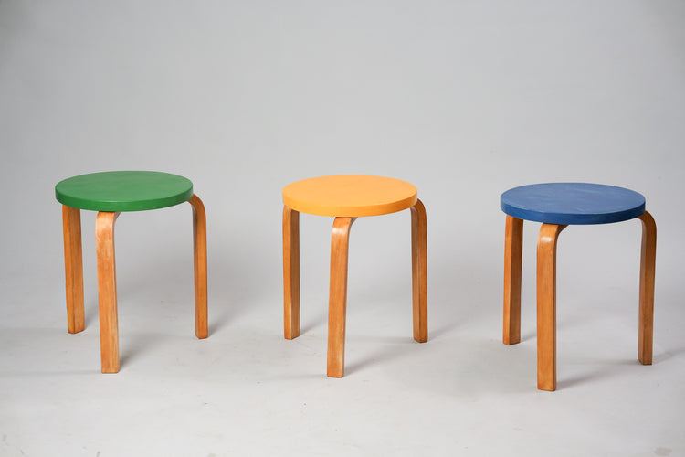 Three stools with three legs. Each of the stools have a circle seat in a different color. One green, one yellow and one blue.