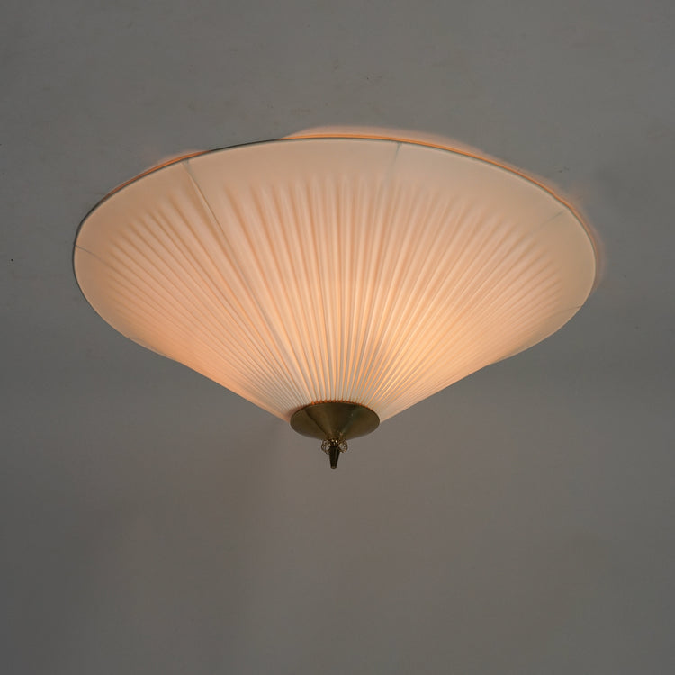 Round white plafond with a plastic shade that has a pleated design. In the middle of the lamp is a brass detailing.