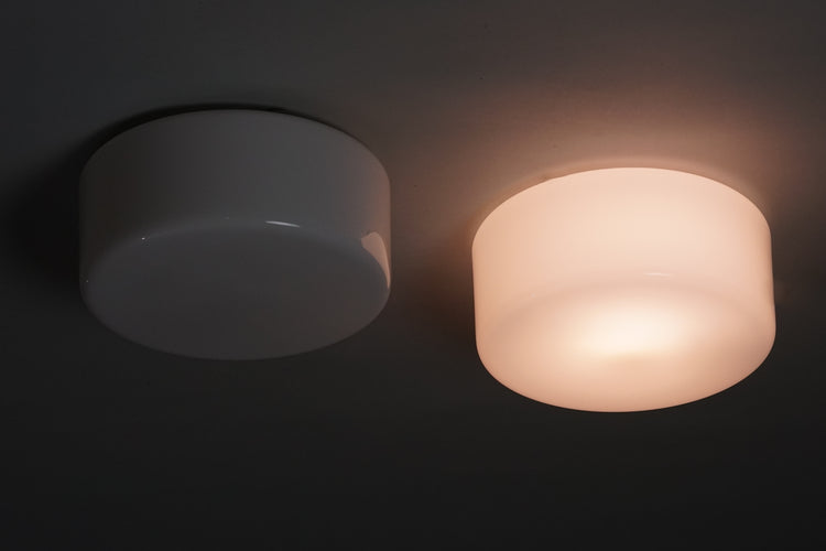 Two identical plafond lamps. The lamps are cylinder shape and white.