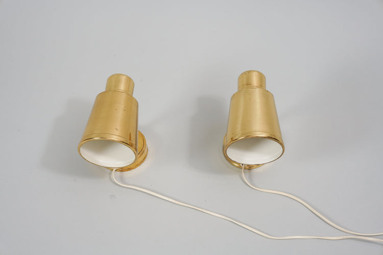 Two identical wall lamps made of brass. In middle of the base is a white switch.