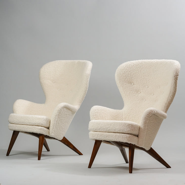 Two white wingback armchairs with round and soft shapes. Legs are dark wood.