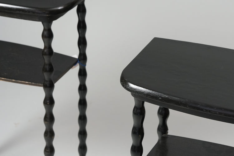 Two identical side tables. Side table is wooden, painted black with a shelf underneath. The legs are a funky wavy design. 