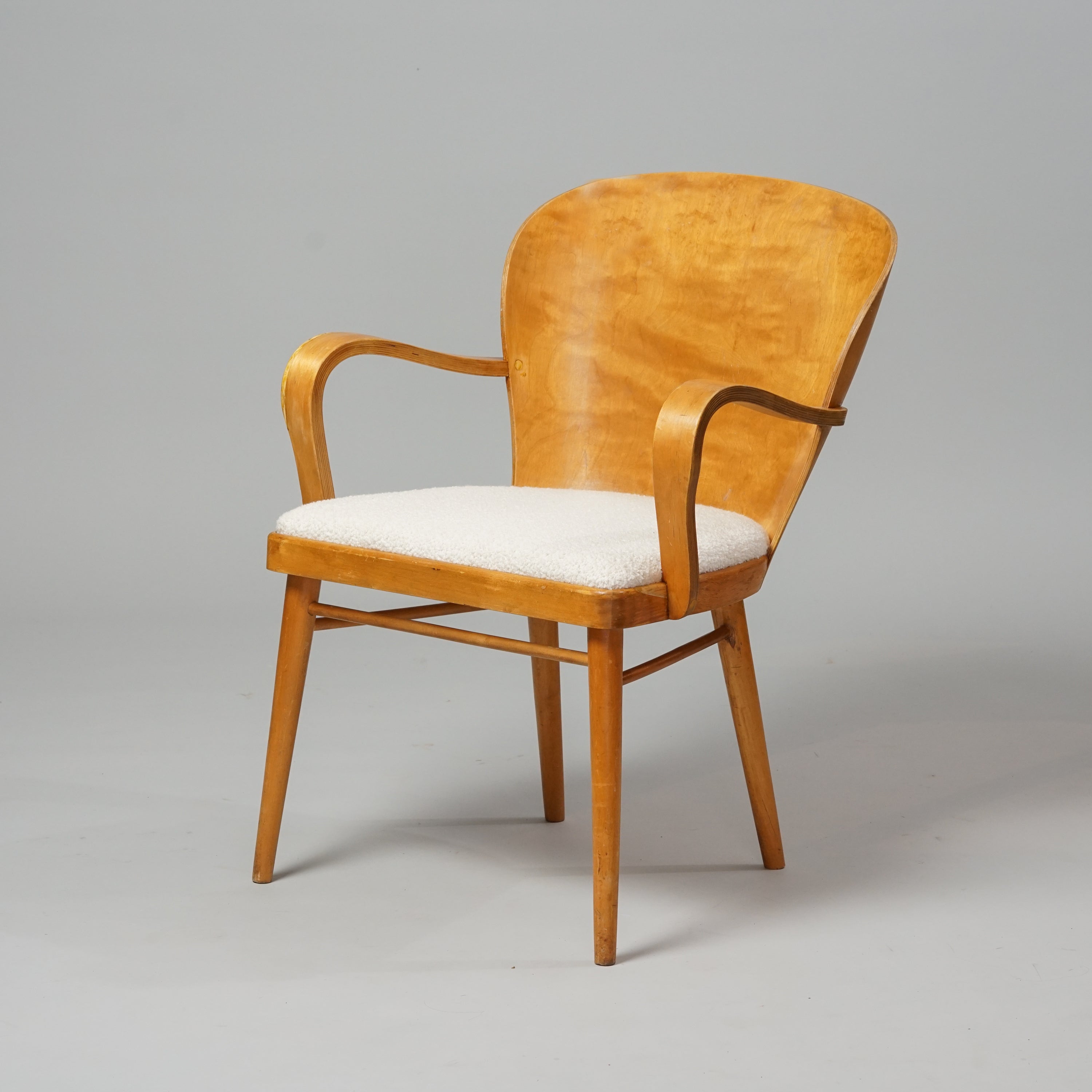 Koivusta tehty tuoli, jossa on leveä kaareva selkänoja. Selkänoja on puinen, ja istuin on verhoiltu valkoisella kankaalla.