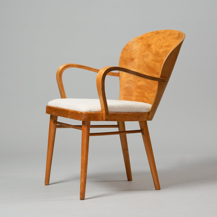 A chair made of birch with a wide curved wooden backrest. The seat is upholstered in white fabric.