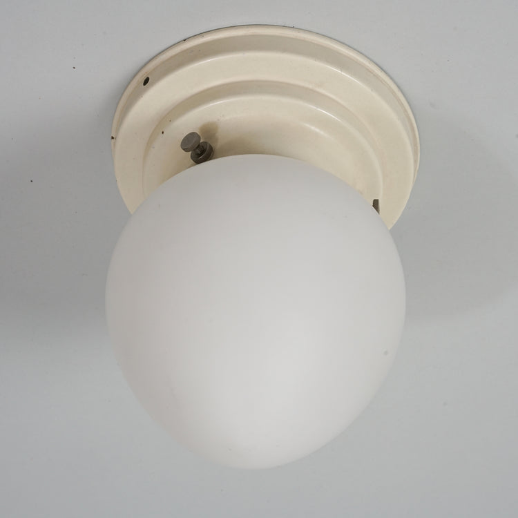 A ceiling lamp with metal frame and white cloudy glass dome which is oval shape.