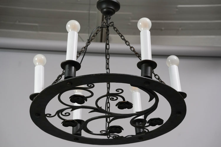 Black iron chandelier with six candle-like lamps. The chandelier has flower design. 