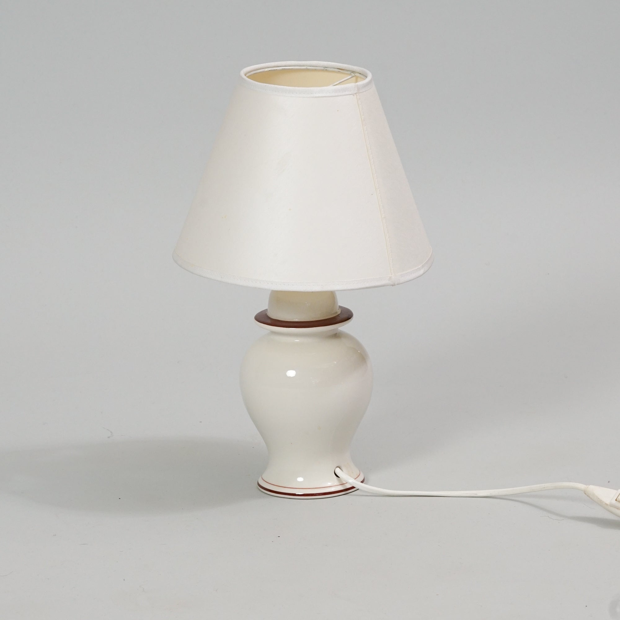 White porcelain lamp with red detailing on the base. The fabric shade is also white.