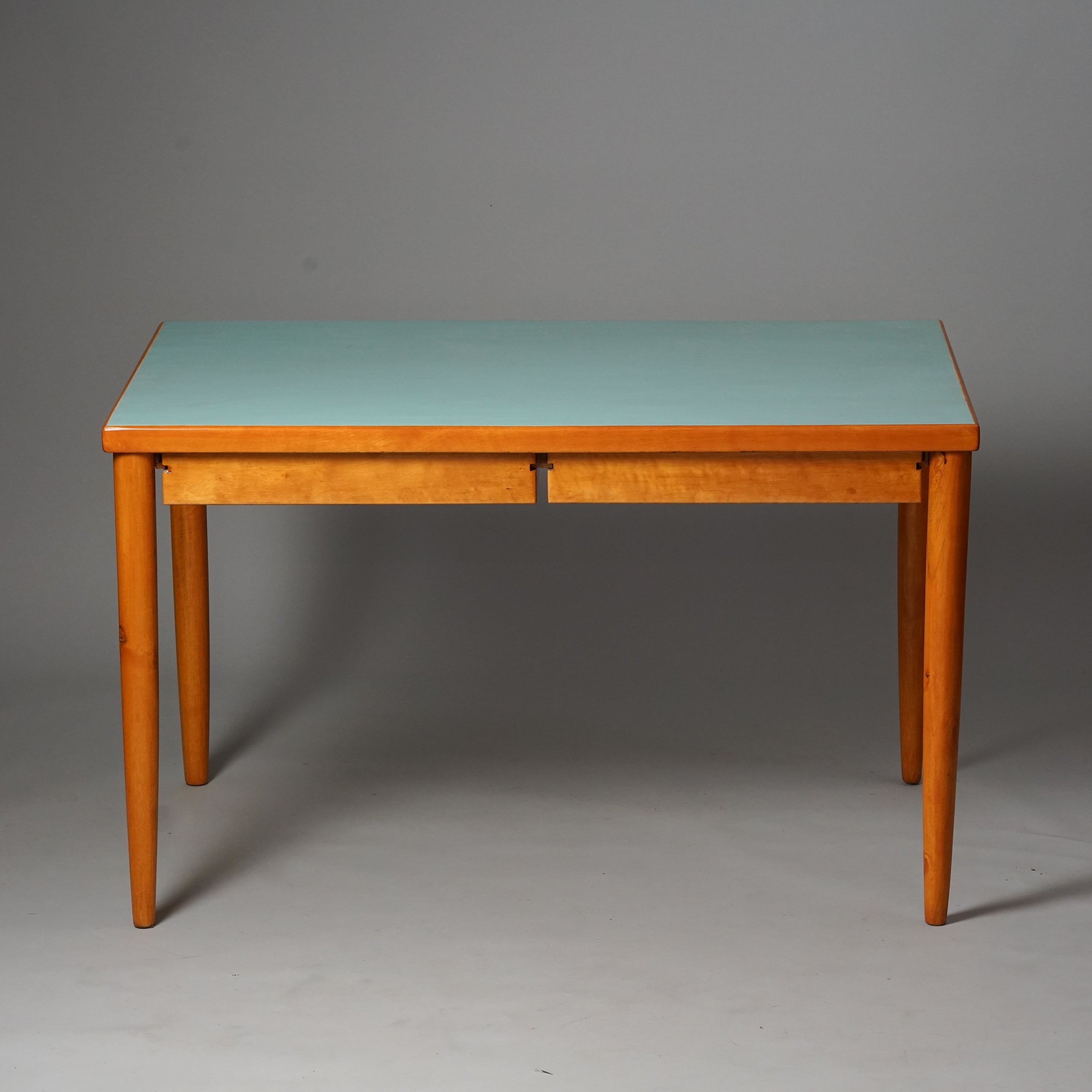 Pöydän työtaso on maalattu vaaleansiniseksi, muuten pöytä on puun värinen. Sisältää kaksi vetolaatikkoa.