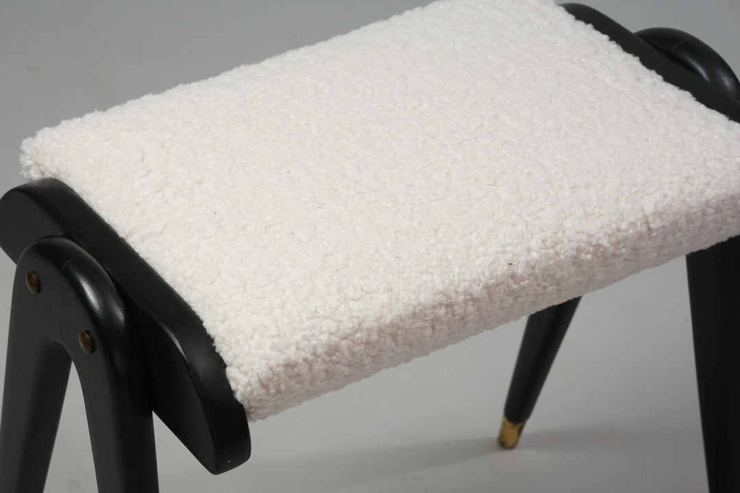 Stool with wooden legs and frame painted black, brass sleeves on the legs and a white fluffy fabric on the seat.