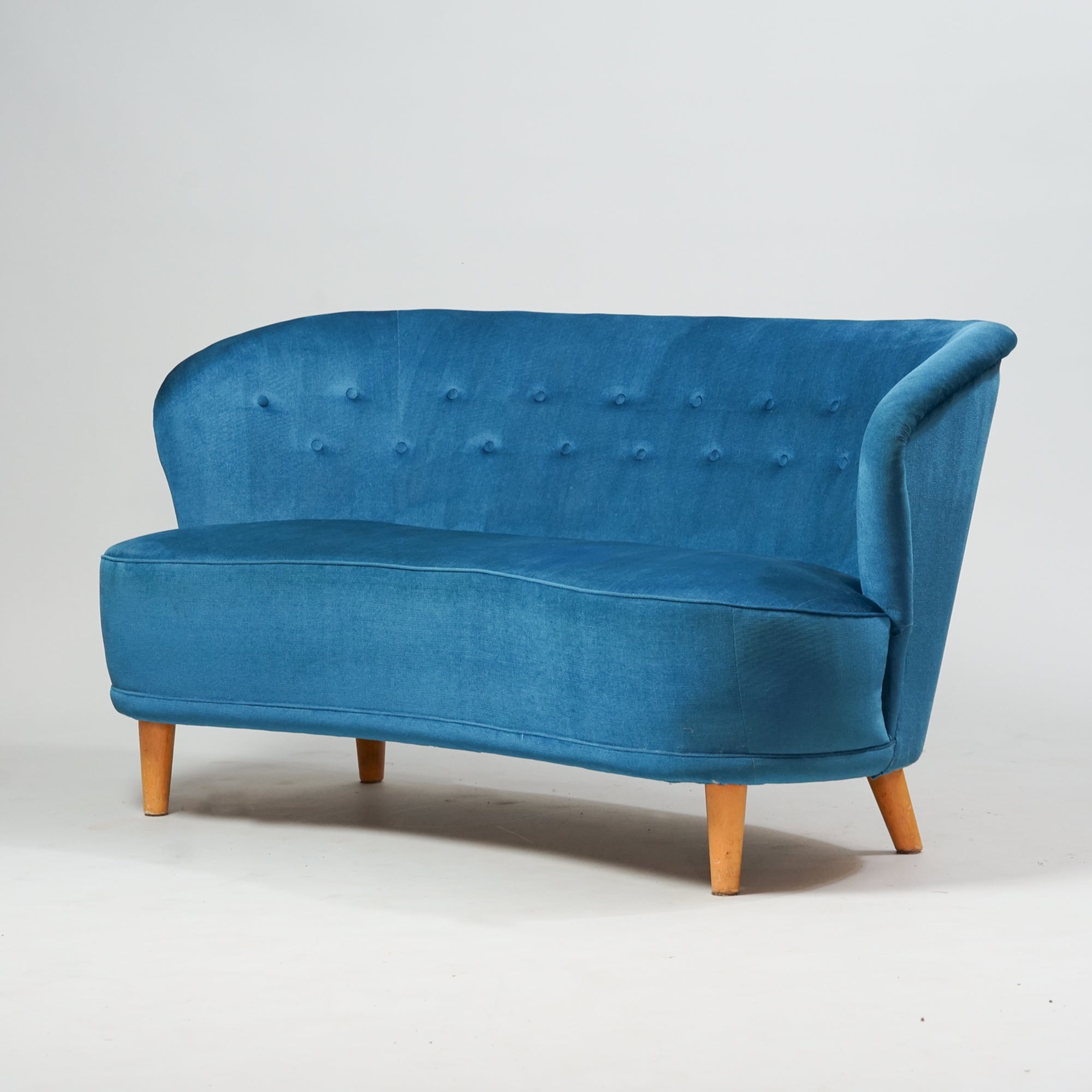 Sininen 2-istuttava kaareva sohva, jossa neljä puista jalkaa.