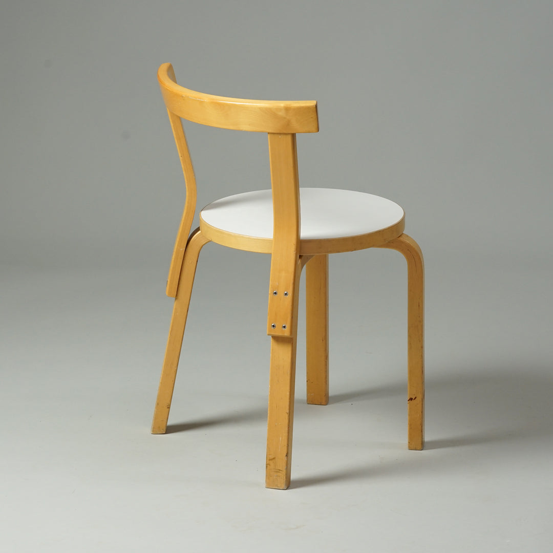 A chair made of birch with four legs and a thin backrest. The seat is round with a white linoleum top.