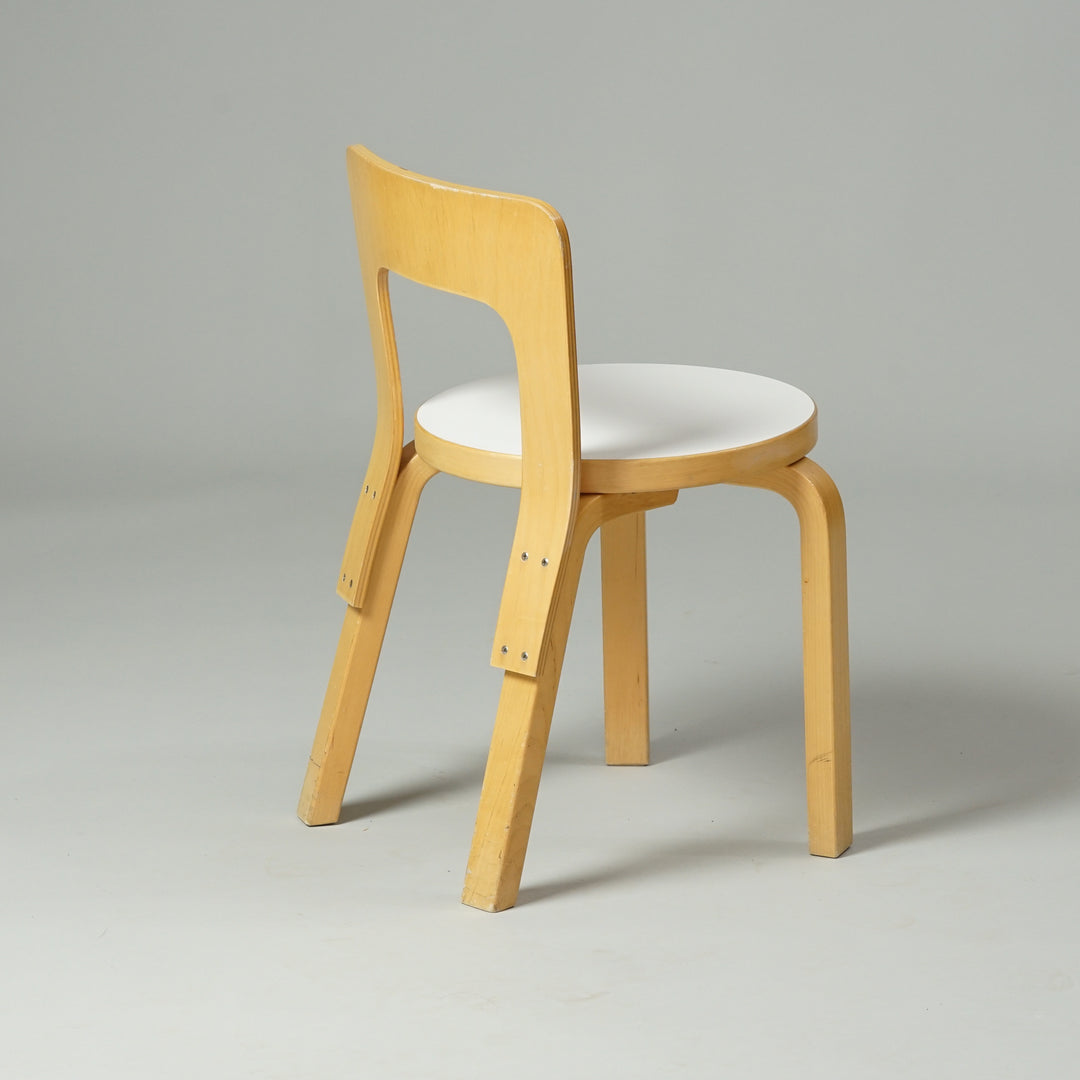 A chair made of birch with four legs and a backrest. The seat is round with a white linoleum top.