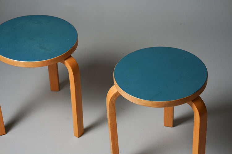 Three legged stool with a birch frame and turquoise linoleum seat. The seat part is round.