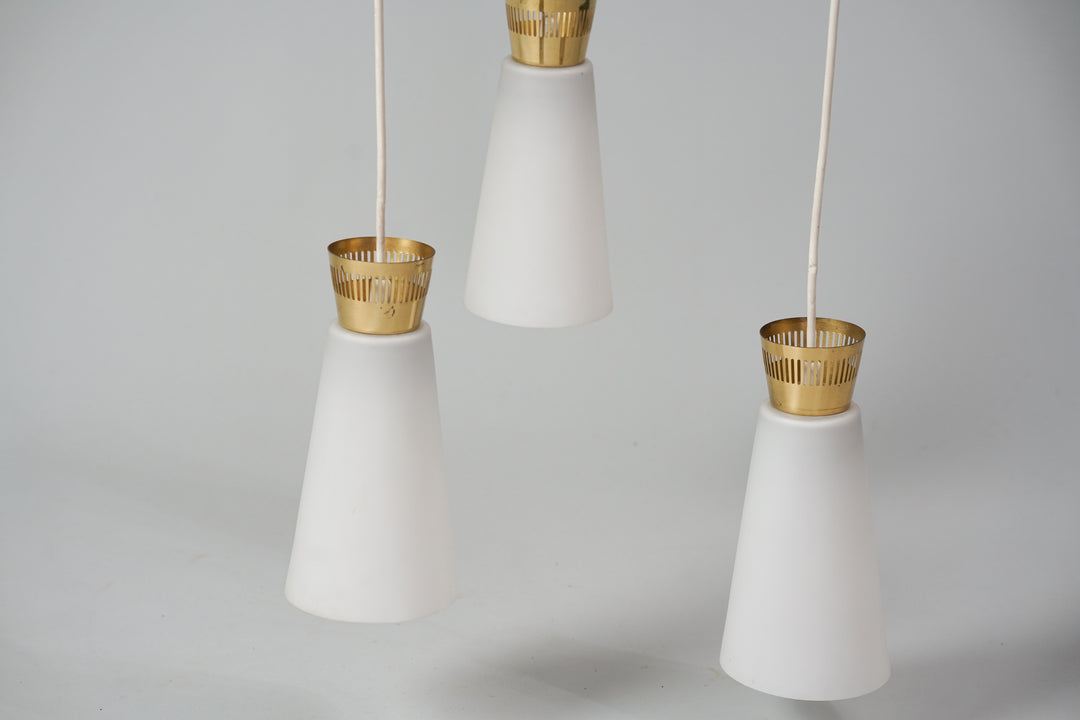 A lamp with three cloudy white glass domes with brass bases. The frame of the lamp is brass. 