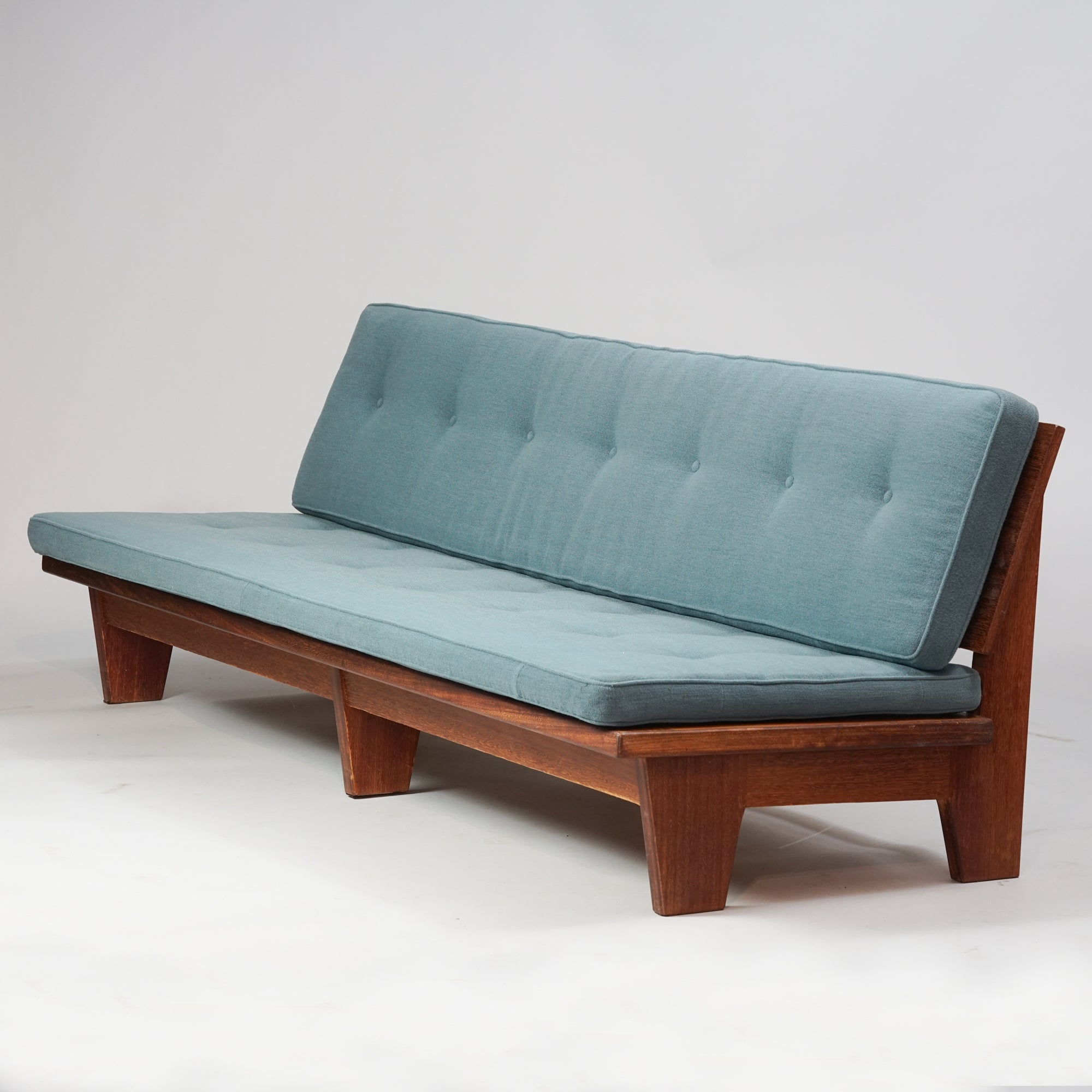 Pitkä sohva, jonka runko tiikkiä ja harmahtavan sininen istuinosa villakangasta.