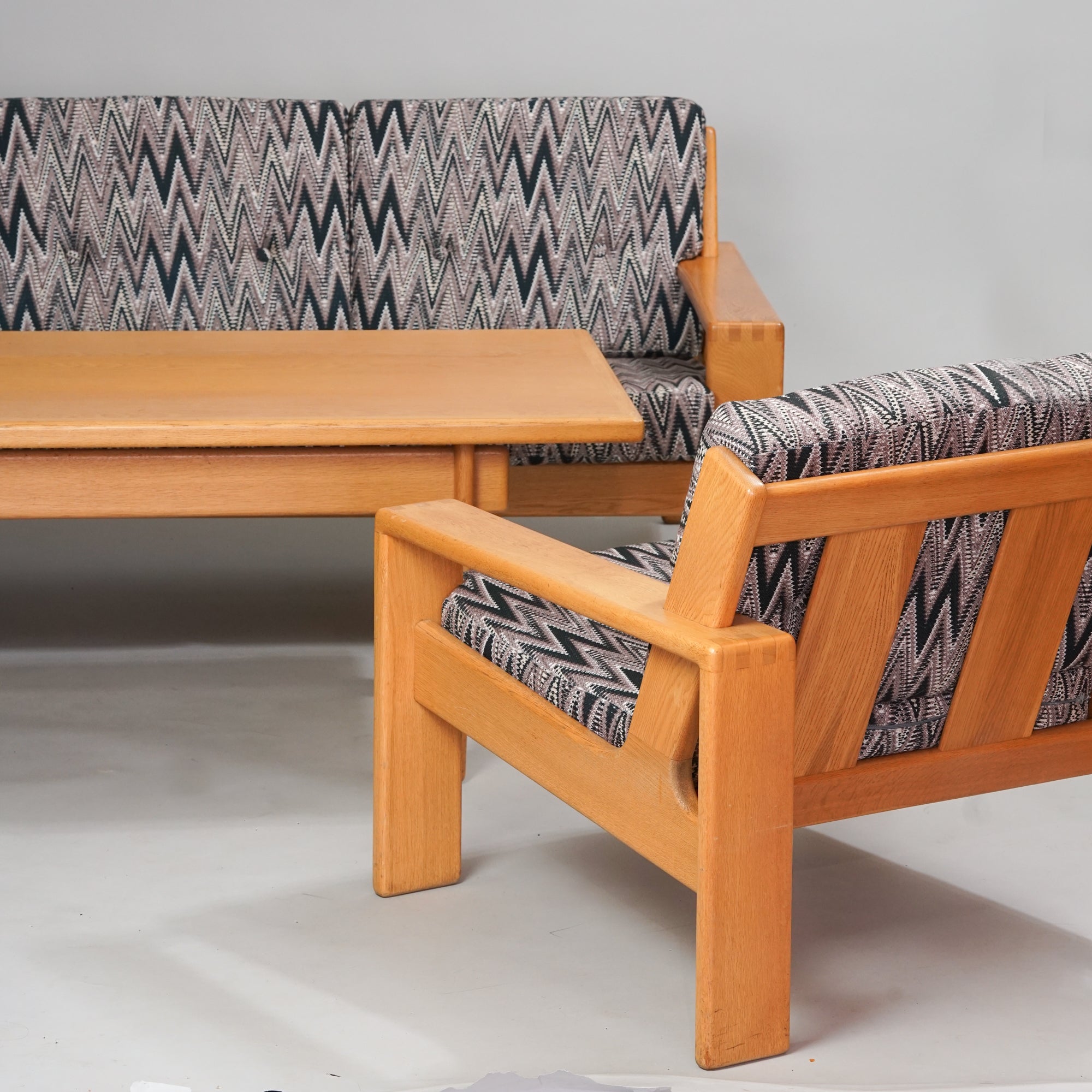 Tammesta tehty sohvapöytä, jonka vieressä on sohva ja kaksi nojatuolia, joiden rungot on tammea. Sohvan ja nojatuolien verhoilu zigzag-kuviointi.