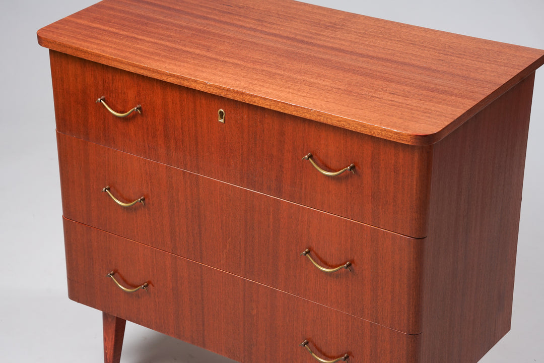 Mahogany chest of drawers, with three drawers. Each drawer has two brass handles, and the top drawer has a keyhole.