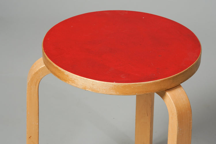 A three legged stool made of birch with a round red linoleum seat.