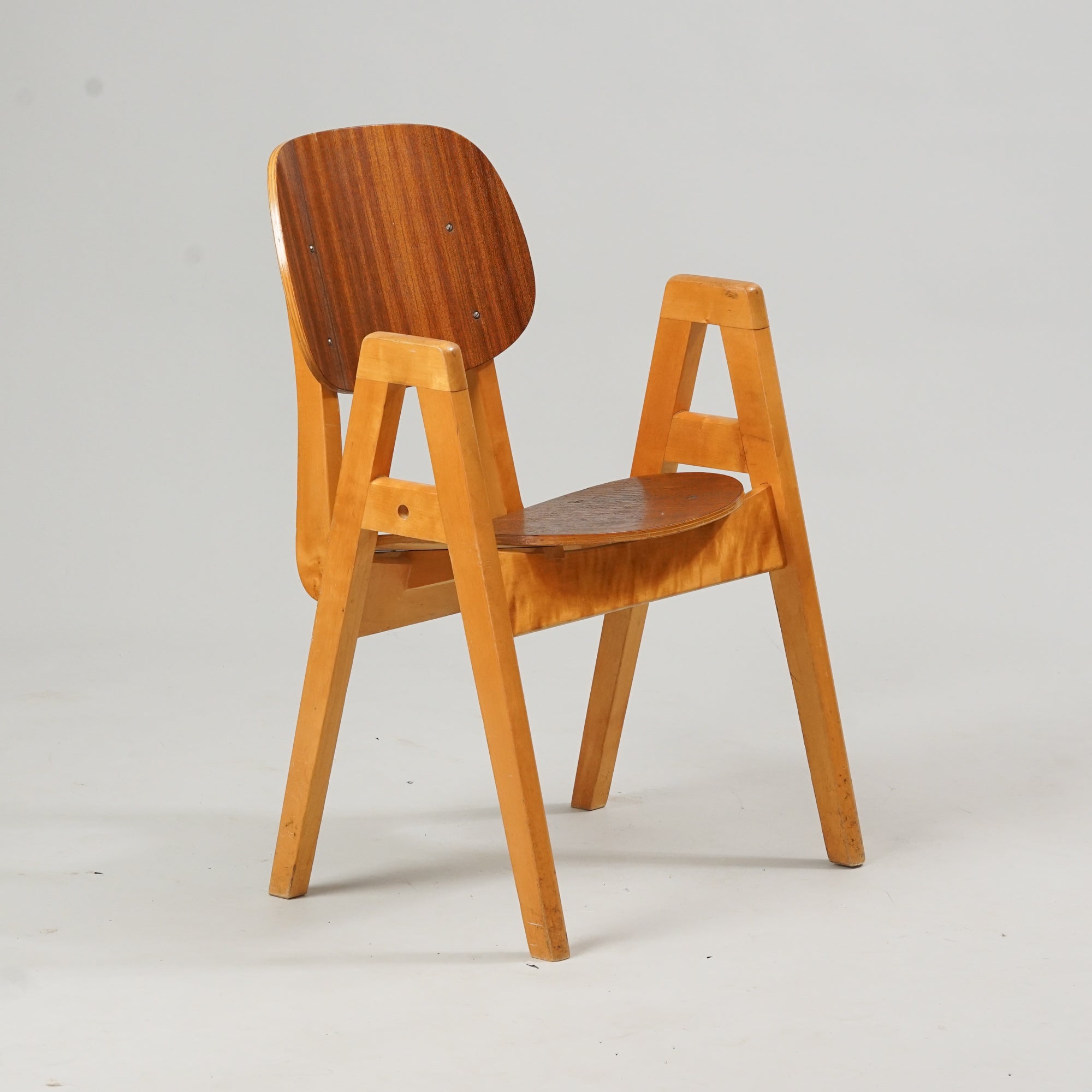 Puusta tehty tuoli, jossa tummempi selkänoja ja istuin. Käsinojat ovat "A"-muotoisia. 
