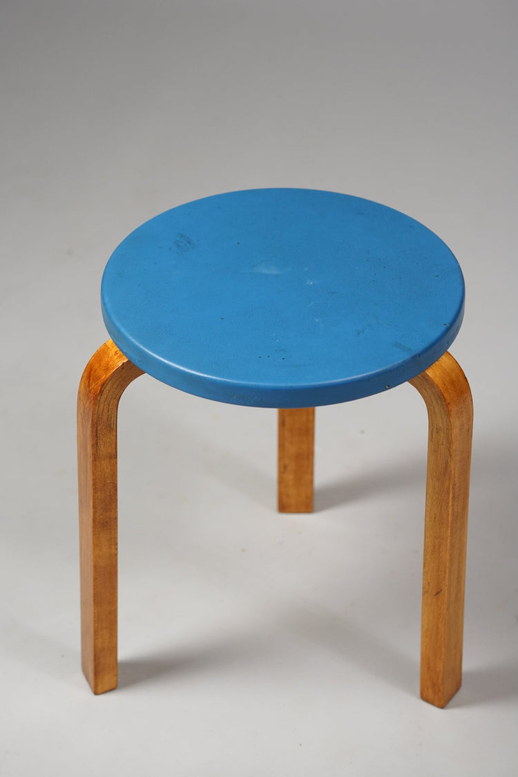 Three legged stool made of birch with a blue round seat.