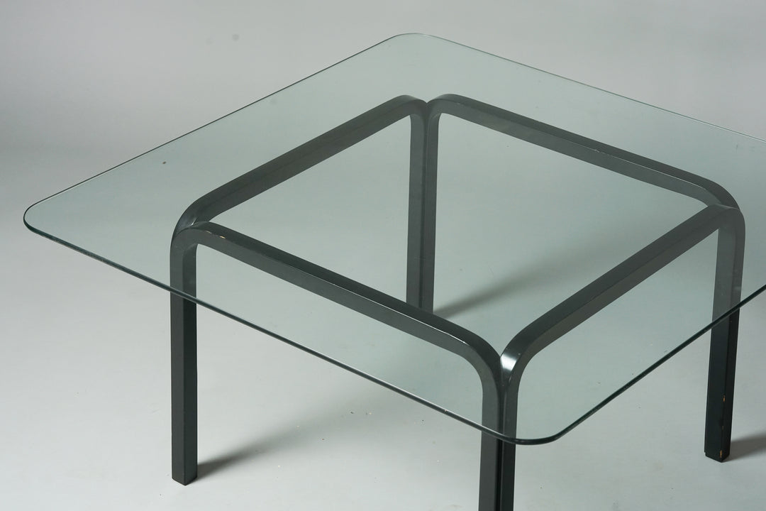 A coffee table with square black painted wood frame and bigger glass table top. 