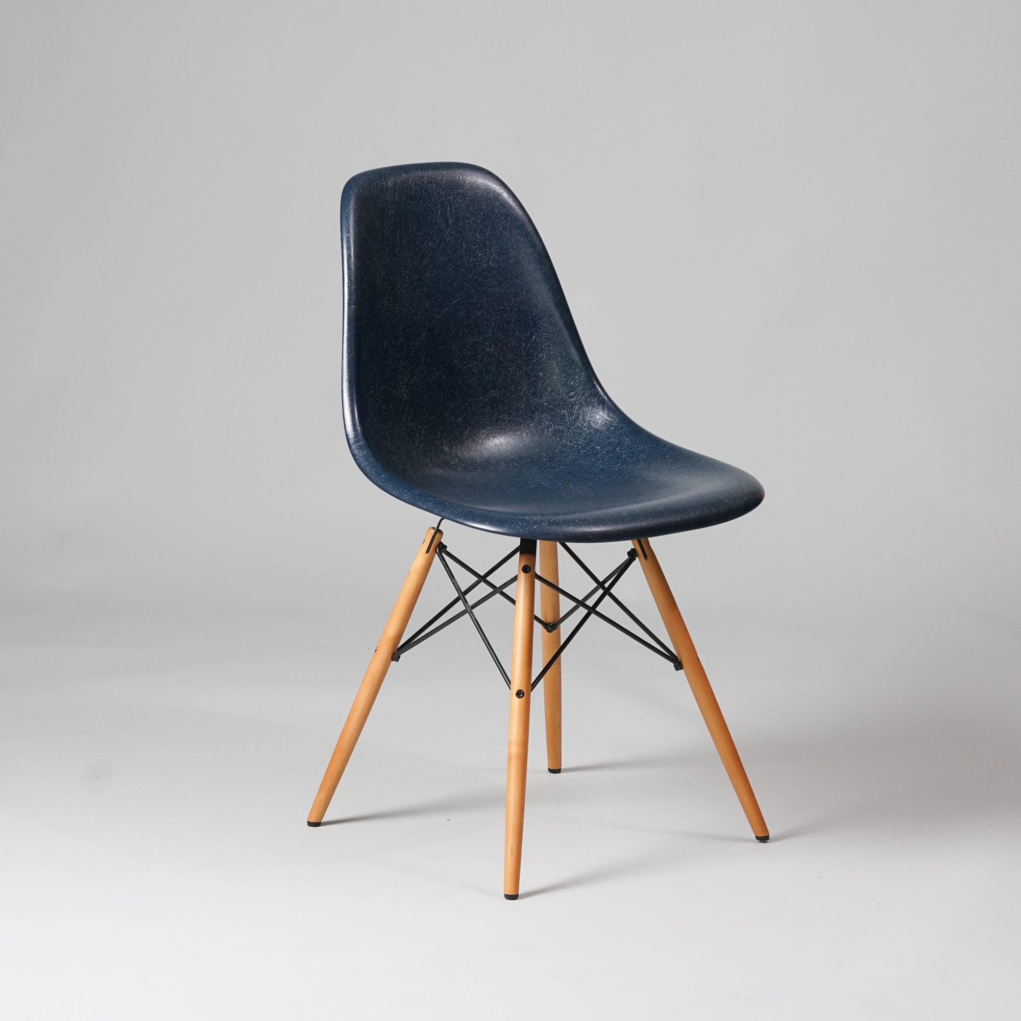 Tuoli, jonka jalat ovat vaahteraa ja jalkojen välissä olevat tangot metallia. Tummansininen istuinosa on lasikuitua.