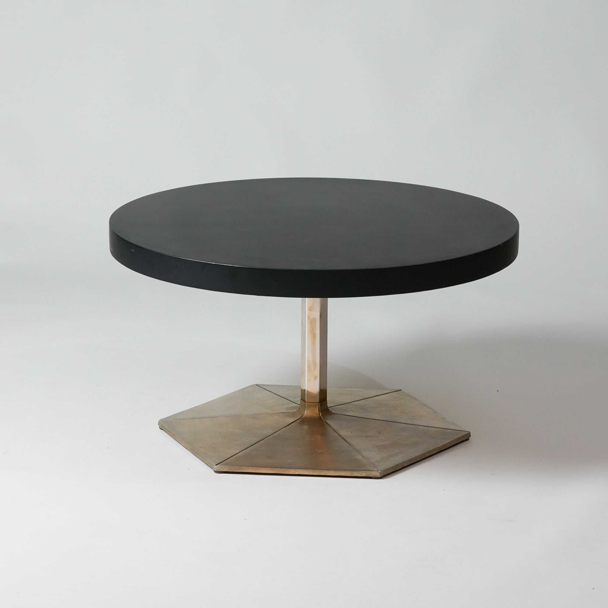 Pyöreä musta puupöytä, jossa kuusikulmion muotoinen metallinen jalka. 