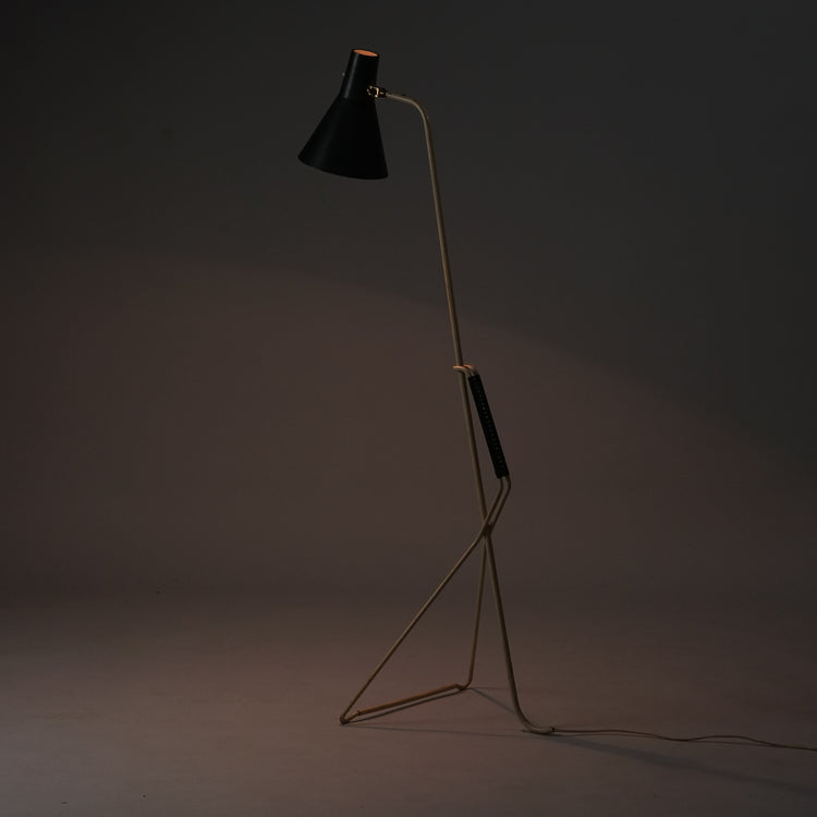 Floor lamp with cream-coloured metal frame, plastic wrapping in the middle of the frame and black metal triangular shade.The lower part of the frame has a triangular shape that holds the lamp upright.