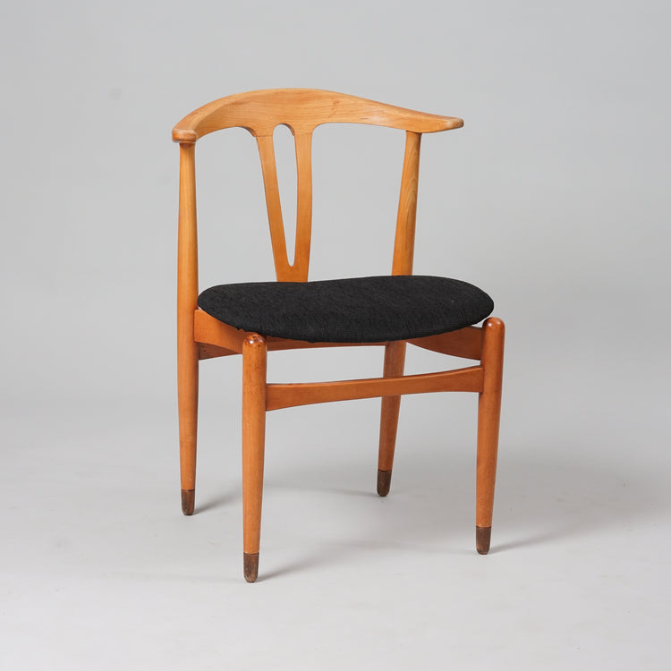 Wooden chair with black fabric upholstery on the seat. The back of the chair consists of a V-shaped piece of wood joined at the upper back to a horizontal piece of wood in the shape of a crescent.