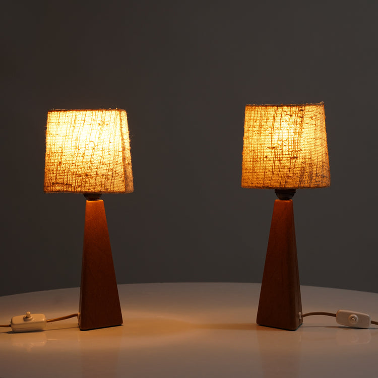 Two identical lamps. the leg of the lamp is brown leather while the fabric shade is beige. The leg is rectangle shape, shrinking when going towards the lamp shade.