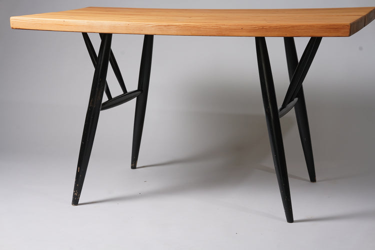 Rectangular dining table with light brown pine top. Four round legs, with support beams for the table top. Legs and supports painted black.