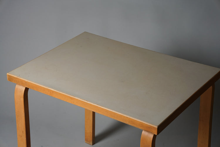 Rectangular table with four birch legs. Table top edges in birch, top in grey linoleum.