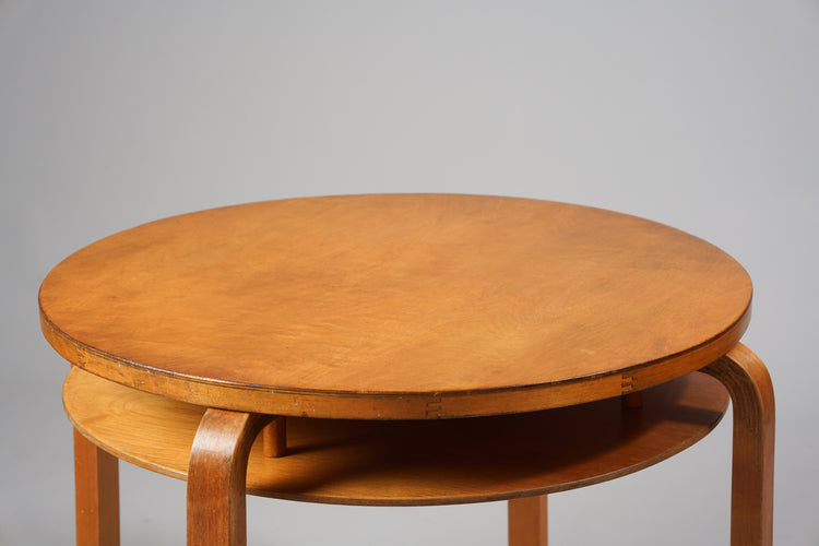 Round wooden table with four legs and a shelf beneath.