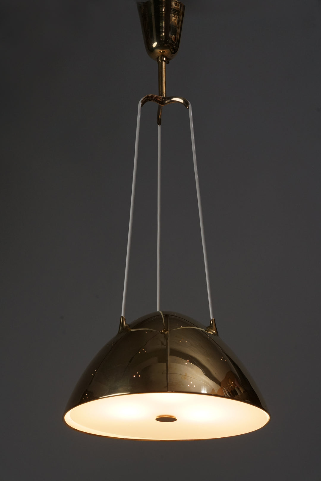 Brass ceiling light. Three white wires branch from the ceiling-mounted part, holding the brass shade of the luminaire. The shade has small three-hole clusters that allow light to escape beautifully from the shade Glass at the bottom of the shade.