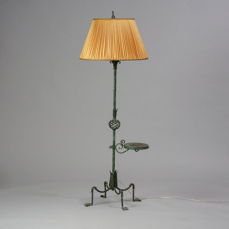 Lamp made of wrought iron with a decorated leg. The leg has a small counter on the side. The shade is made of yellow fabric.