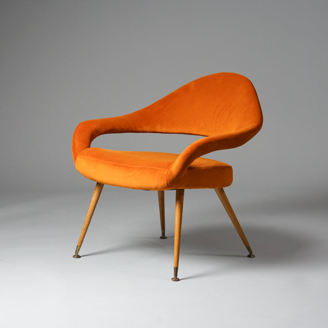 Ainutlaatuinen oranssi nojatuoli, jonka muoto on kaareva ja pehmeä. Tuolin jalat ovat tehty puusta.