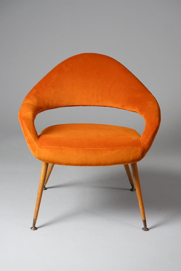 Unique orange armchair, that has a curvy and soft shape. The legs are made of wood.