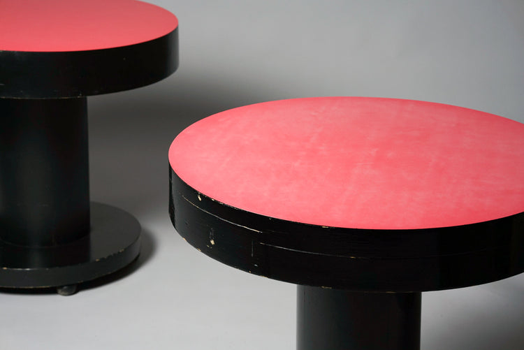 Round table with a soft red tabletop. The table is otherwise black and has four wheels.