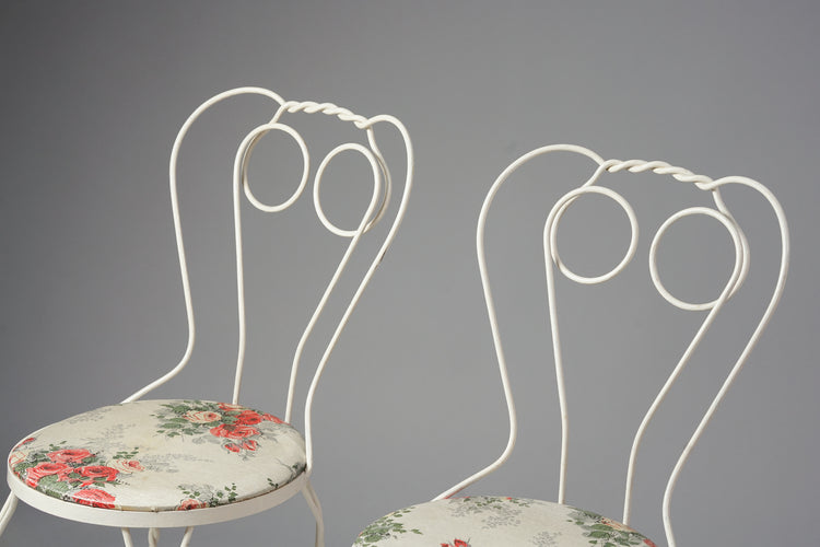 Three white metal chairs. The seats are artificial material and have flower decorations.