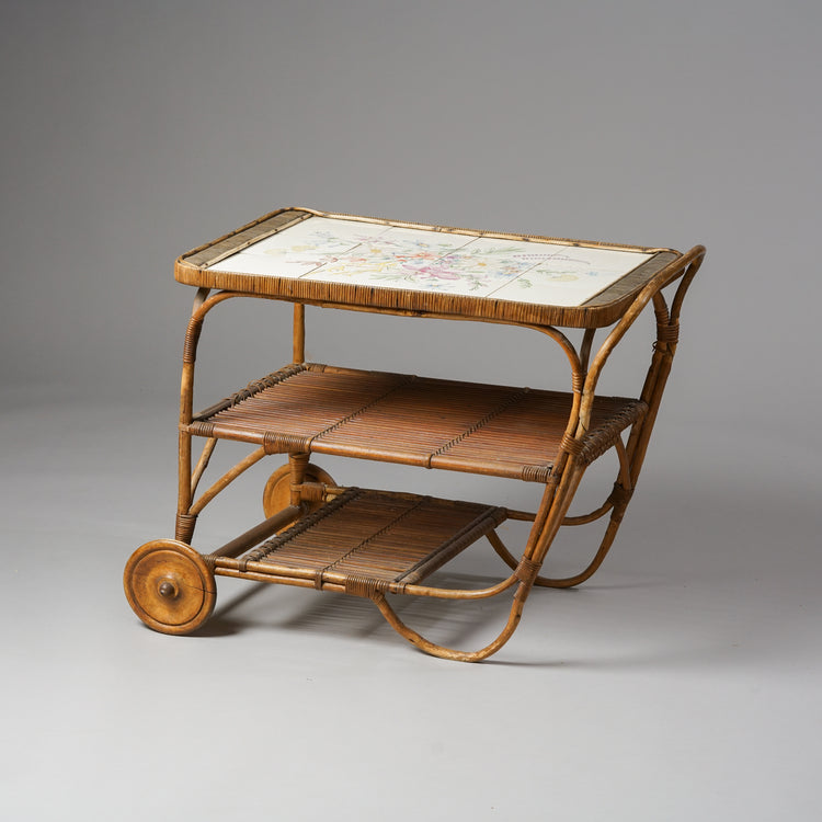Wooden serving trolley with two shelves and a tile top. The trolley has two wheels.