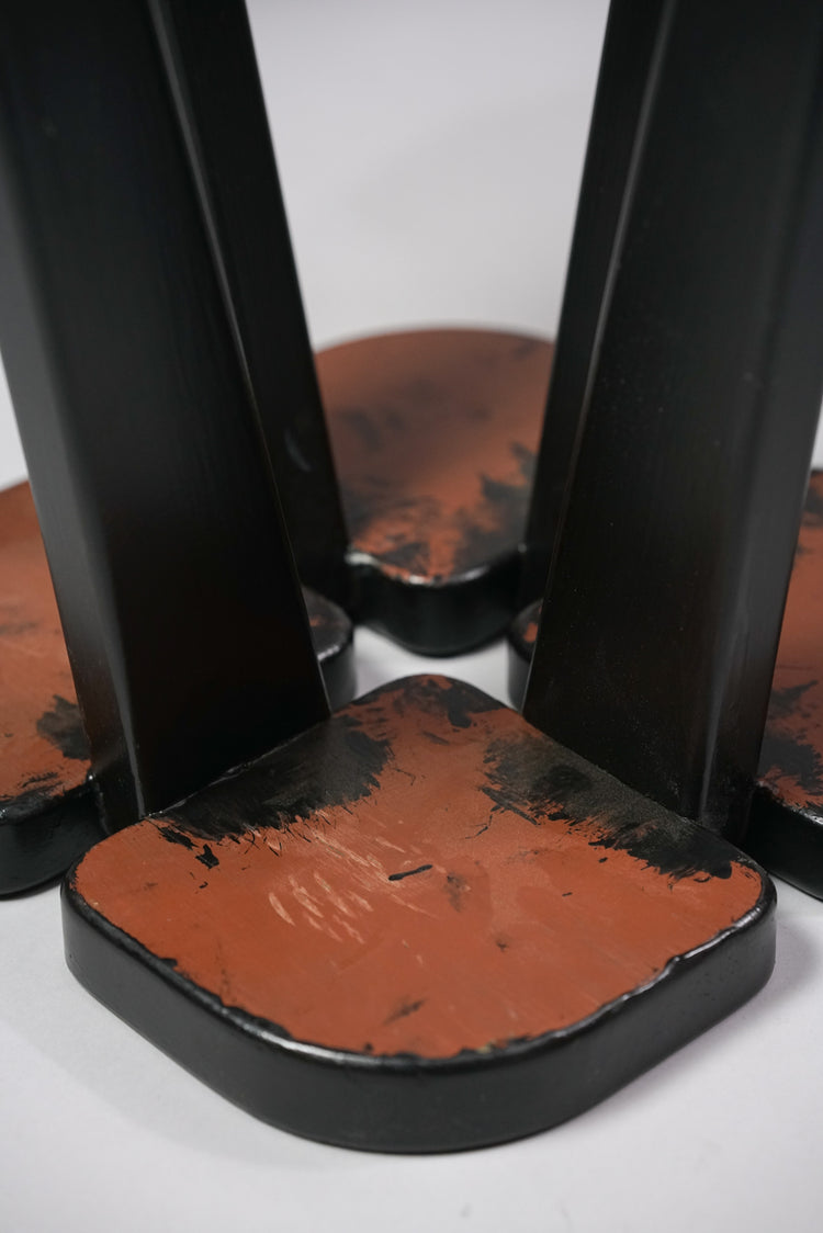 Four identical stools. The stool's seat is in a shape of a four-leaf clover, and has four legs. The stool has been painted black, but the bottom is brown in color. 